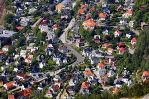 Flyfoto av tett boligområde med hus, hager, veier og jernbane
