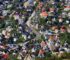 Flyfoto av tett boligområde med hus, hager, veier og jernbane