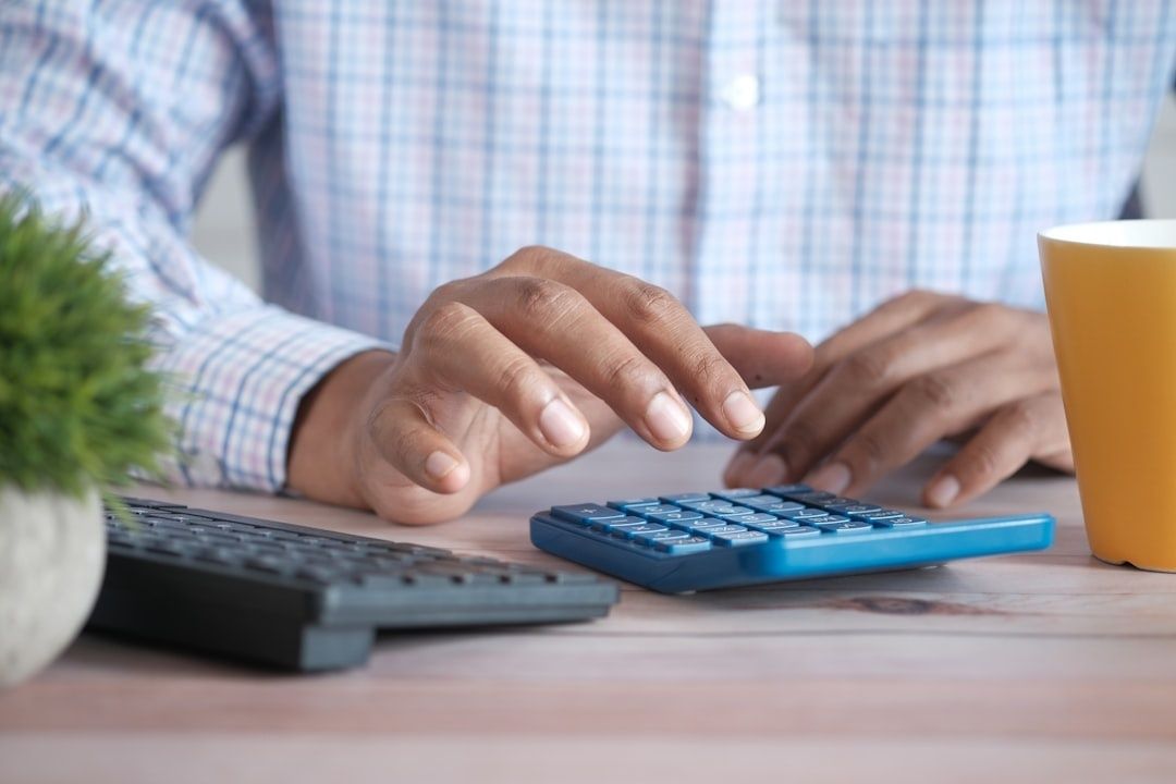 Person bruker kalkulator ved siden av tastatur og kaffekopp