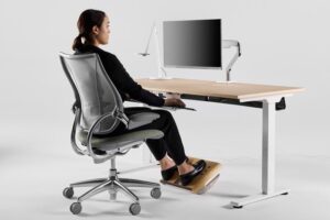 Person ved ergonomisk hjemmekontor med hev-senk-pult og skjerm