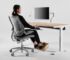 Person ved ergonomisk hjemmekontor med hev-senk-pult og skjerm